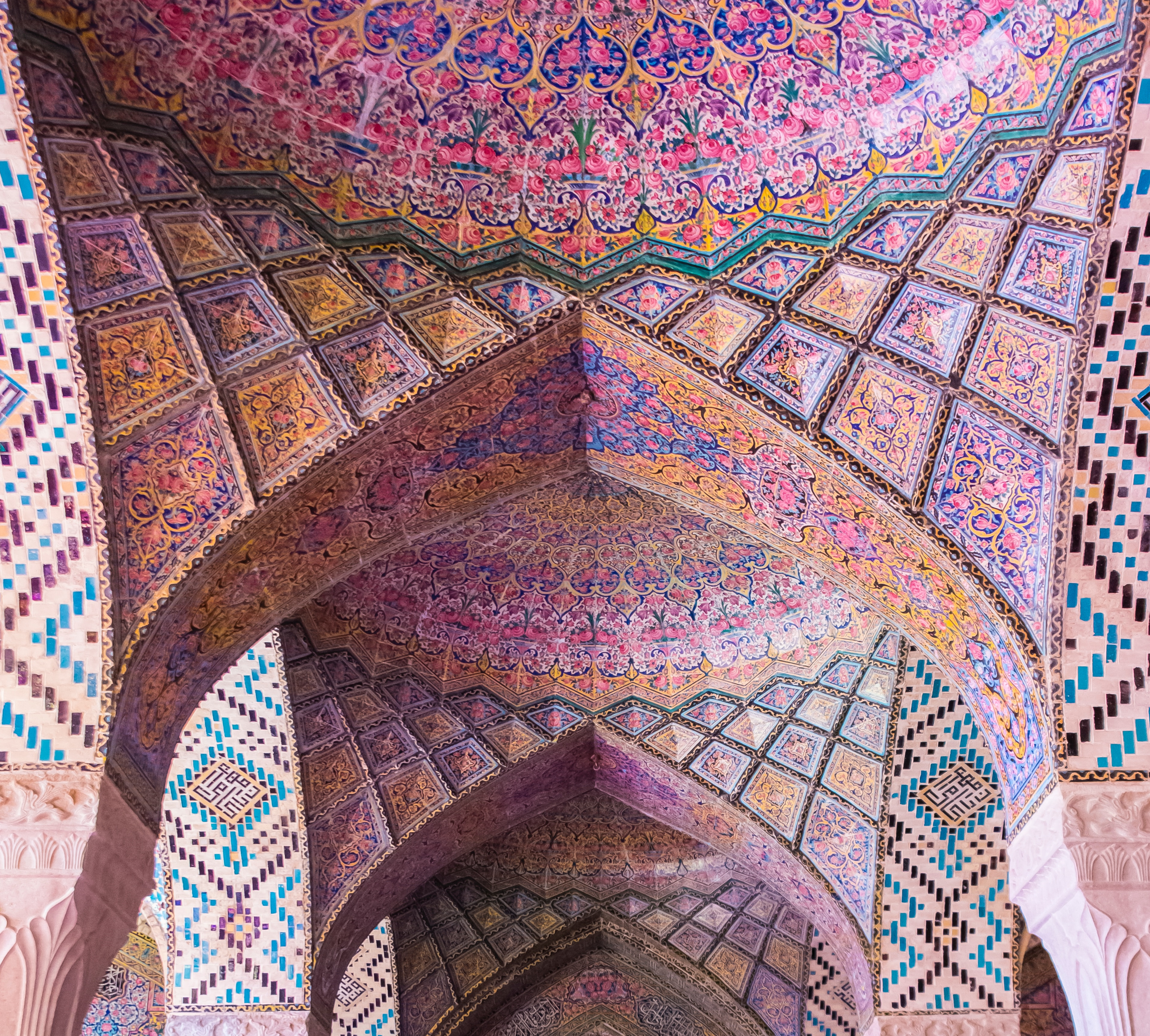 A photograph of an intricately painted vaulted ceiling, as found in old temples, cathedrals and synagogues. Dominant colors are pink and purples with golden yellow and blue. Photograph taken by Faruk Kaymak.