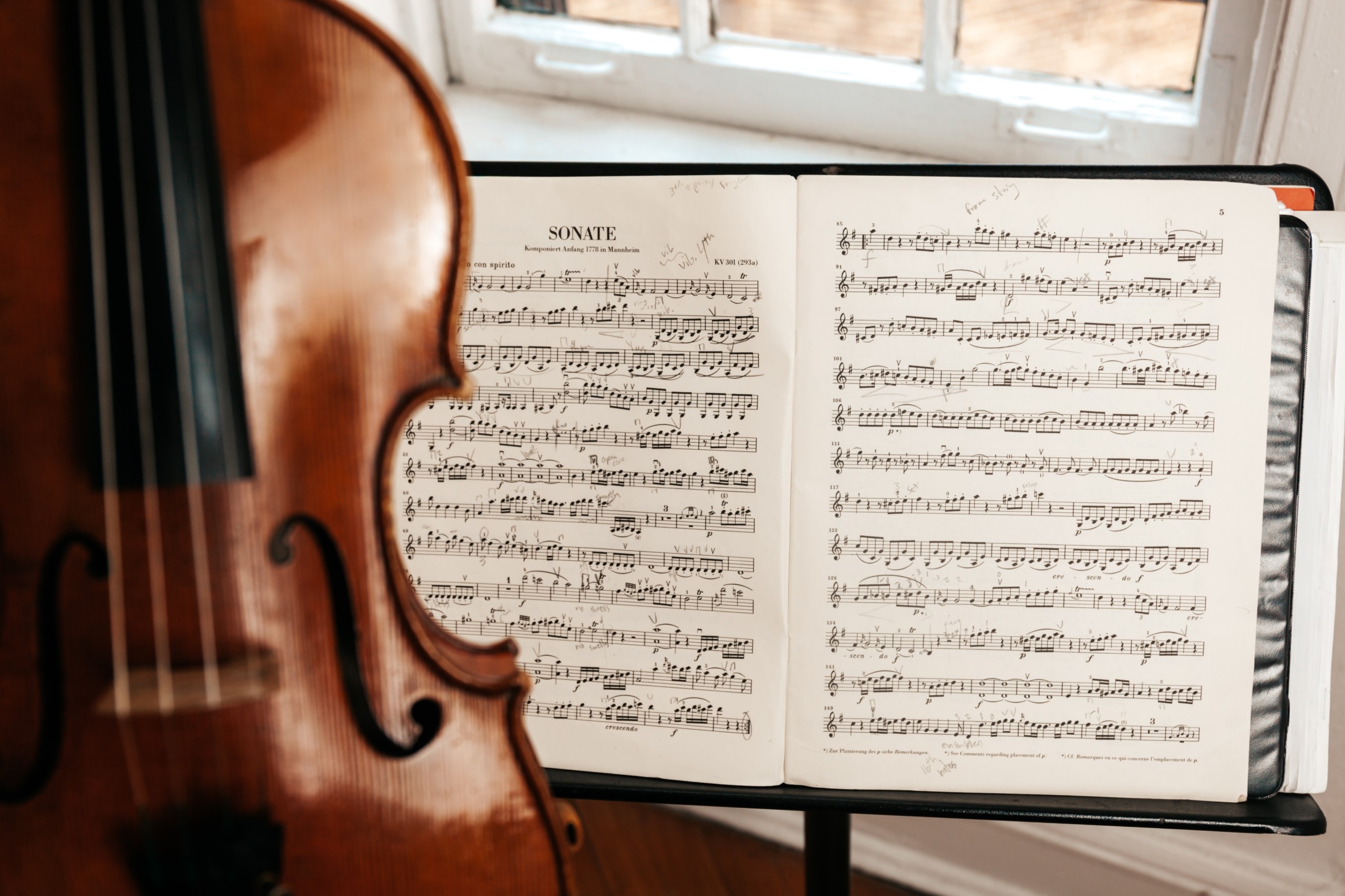 A photograph of a standard black music stand with an open piece of sheet music entitled "Sonate." In the foreground is a s vertically-oriented violin. The photo was taken by Jonathan J. Castellon.