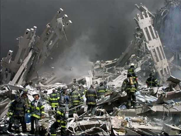 This is a photo of the smoldering girders of the fallen World Trade Center towers in the aftermath of the disaster on September 11, 2001. Only firefighters in their iconic black, yellow-striped jackets and hard hats are allowed to search for survivors.